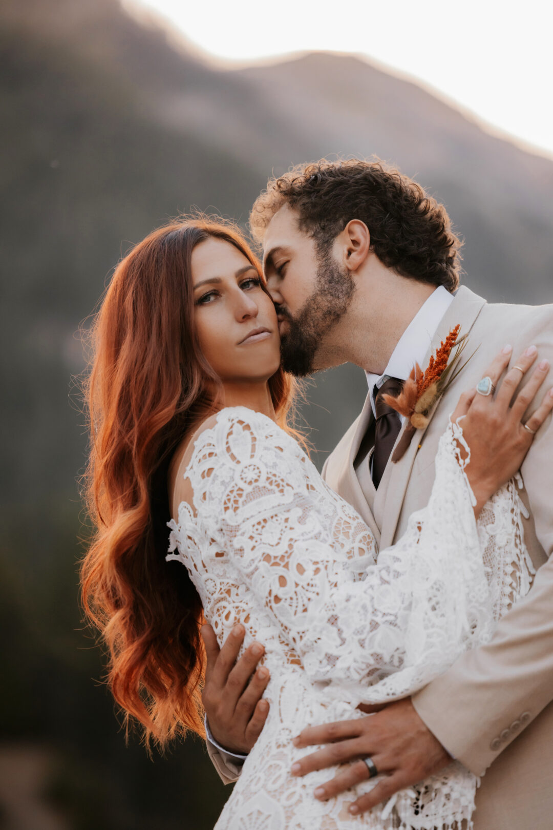 groom kissing bride while she is looking at photographer