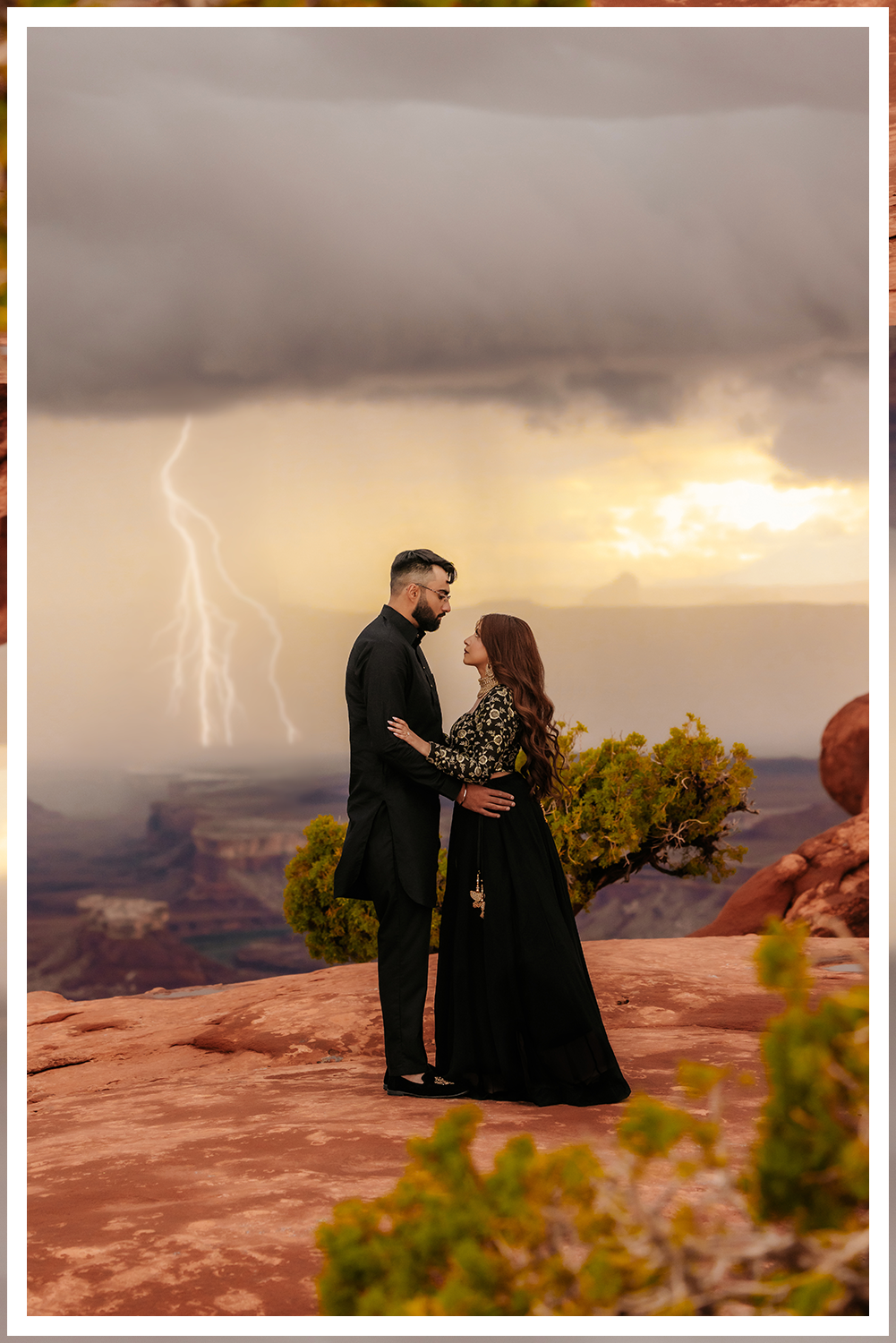 A bride and groom in ornate Indian clothing with a vast desert landscape with stormy skies and lighting with dreamy sunset lighting.