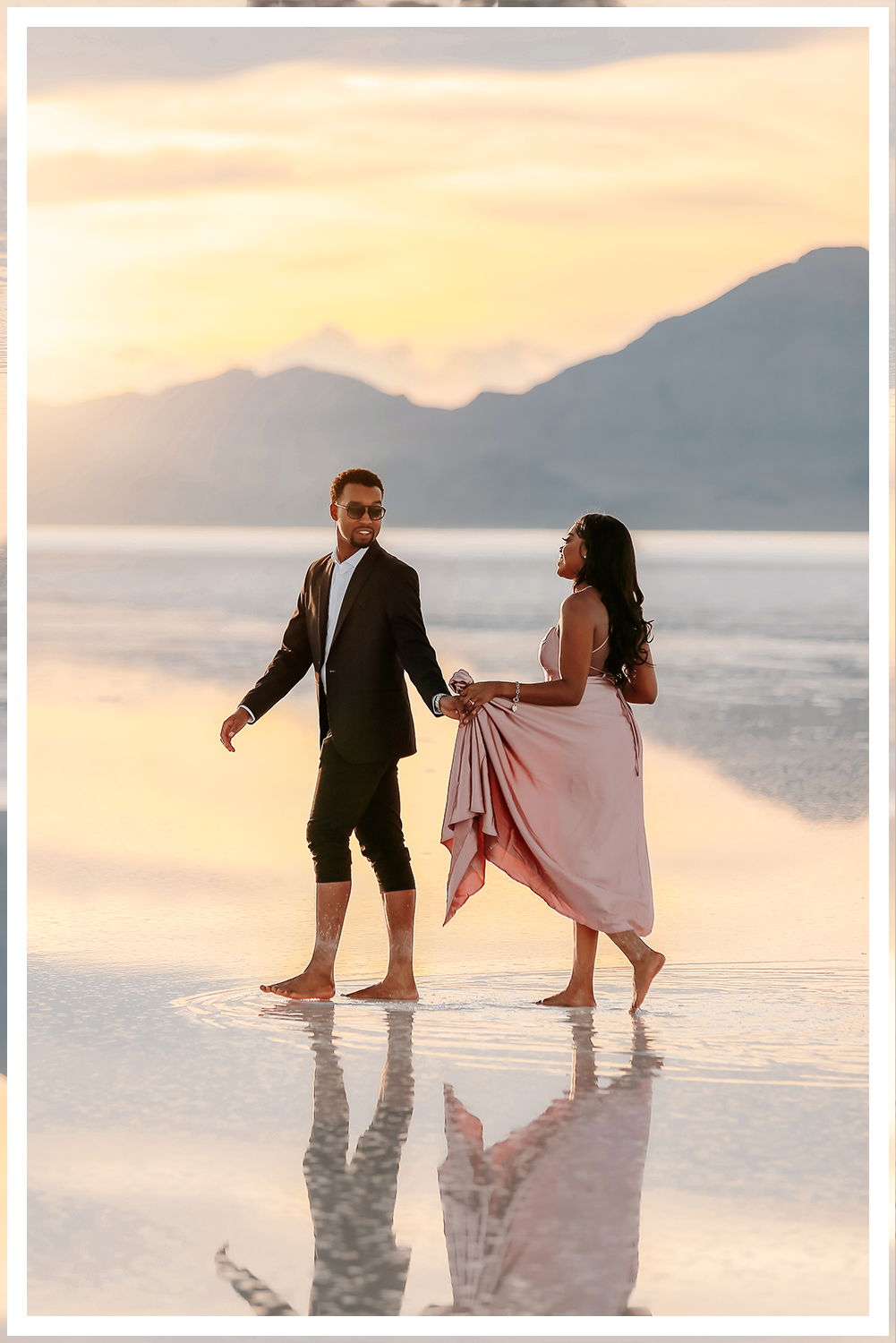 A wedding couple in Dead Horse State Park standing on a large stack of deep red stone at sunset with cinematic hazy lighting near the edge of the cliff.