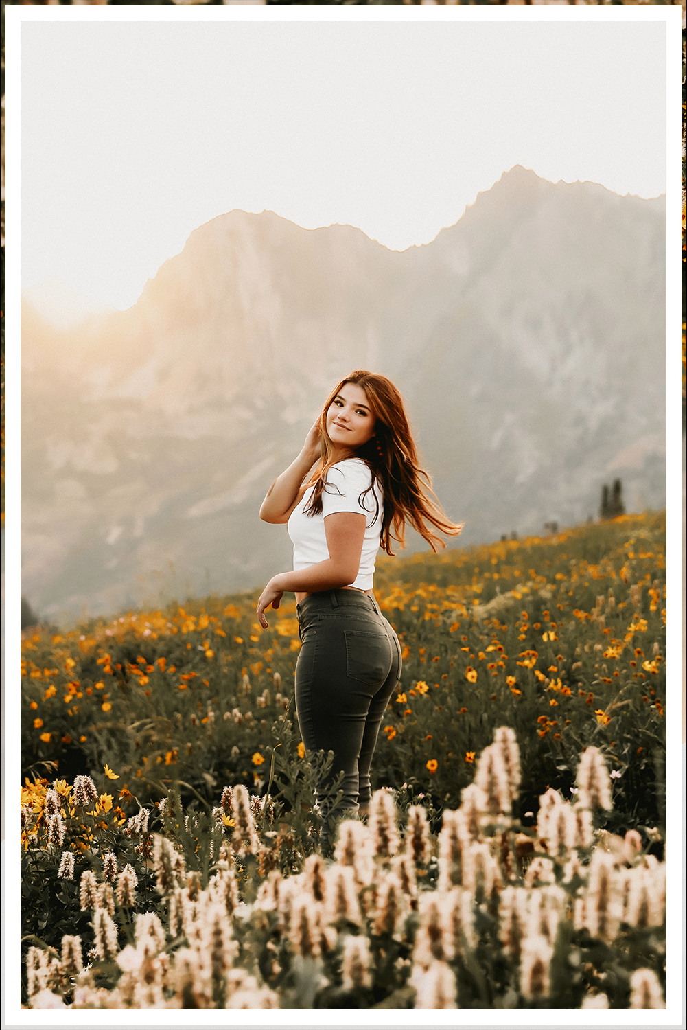 A wedding couple in Dead Horse State Park standing on a large stack of deep red stone at sunset with cinematic hazy lighting near the edge of the cliff.